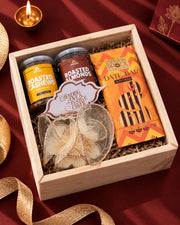 Open pinewood box with saffron cashew and almond jars, a date bar and a gold-net wrapped candle — Aakar Diwali gift hamper