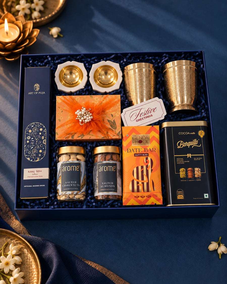 Open navy box from above with brass glasses, marble diyas, salted nut jars and a chocolate tin — Reva Diwali gift hamper