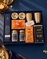 Open navy box from above with brass glasses, marble diyas, salted nut jars and a chocolate tin — Reva Diwali gift hamper